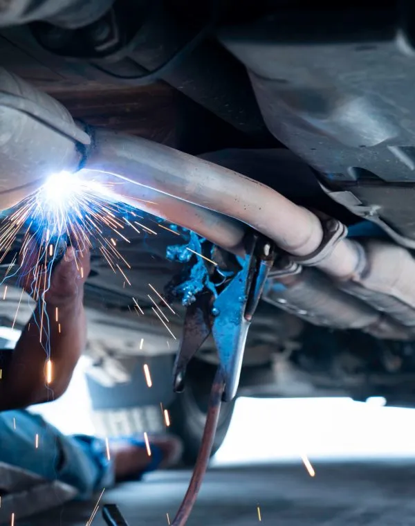 The Hand Of A Mechanic Or Welder Is Fixing A Car Exhaust System By Welding The Exhaust Pipe